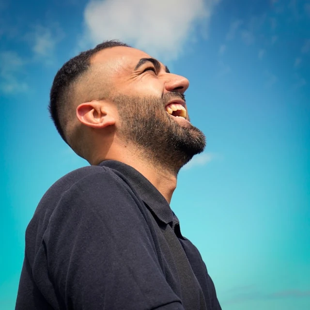 Man with a beard looking up against a clear blue sky