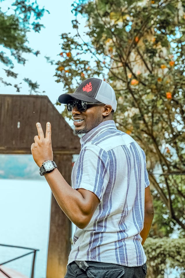 Man making a peace sign outdoors with trees and a building in the background