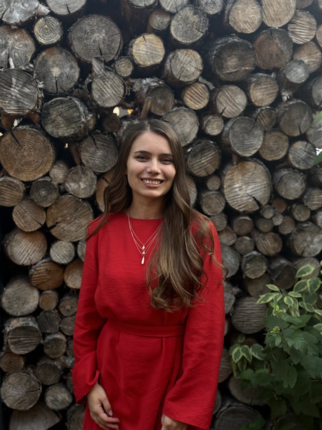 Woman in a red outfit standing in front of stacked wooden logs