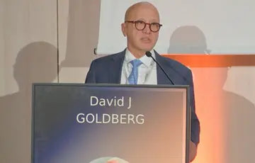 Man at a podium with a screen displaying 'David J Goldberg' in the background