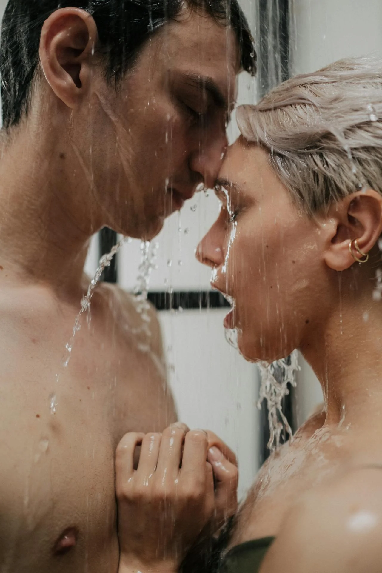 Two people sharing a moment under a shower with water droplets around them.
