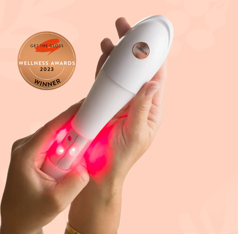 Hand holding Cosara device emitting red light with 'Get the Gloss Wellness Awards 2023 Winner' badge on a peach background.